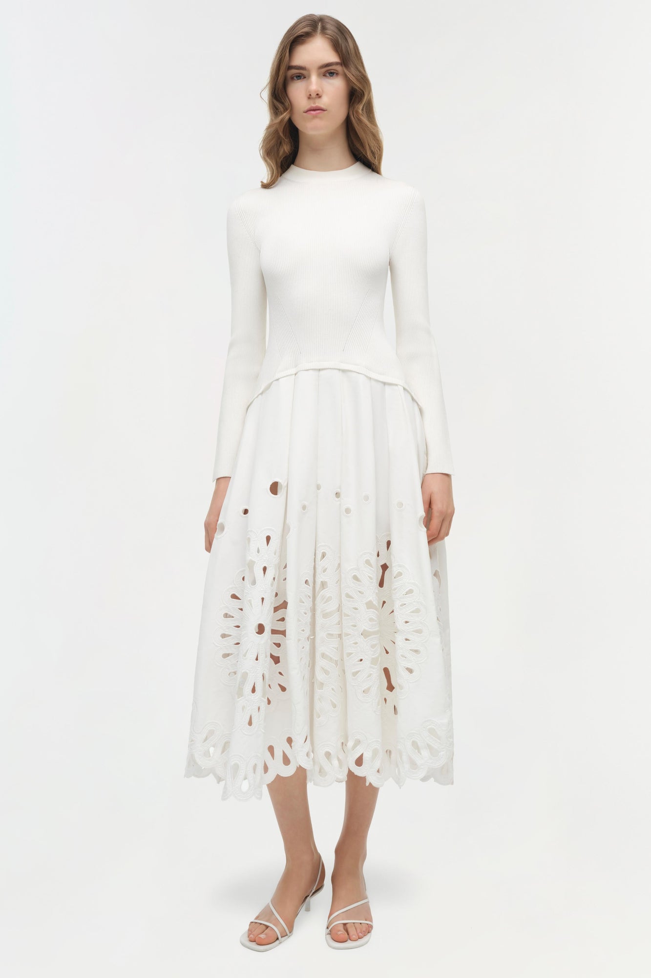 Woman wearing cream knit midi dress with long sleeves and cutout embroidered skirt detail.