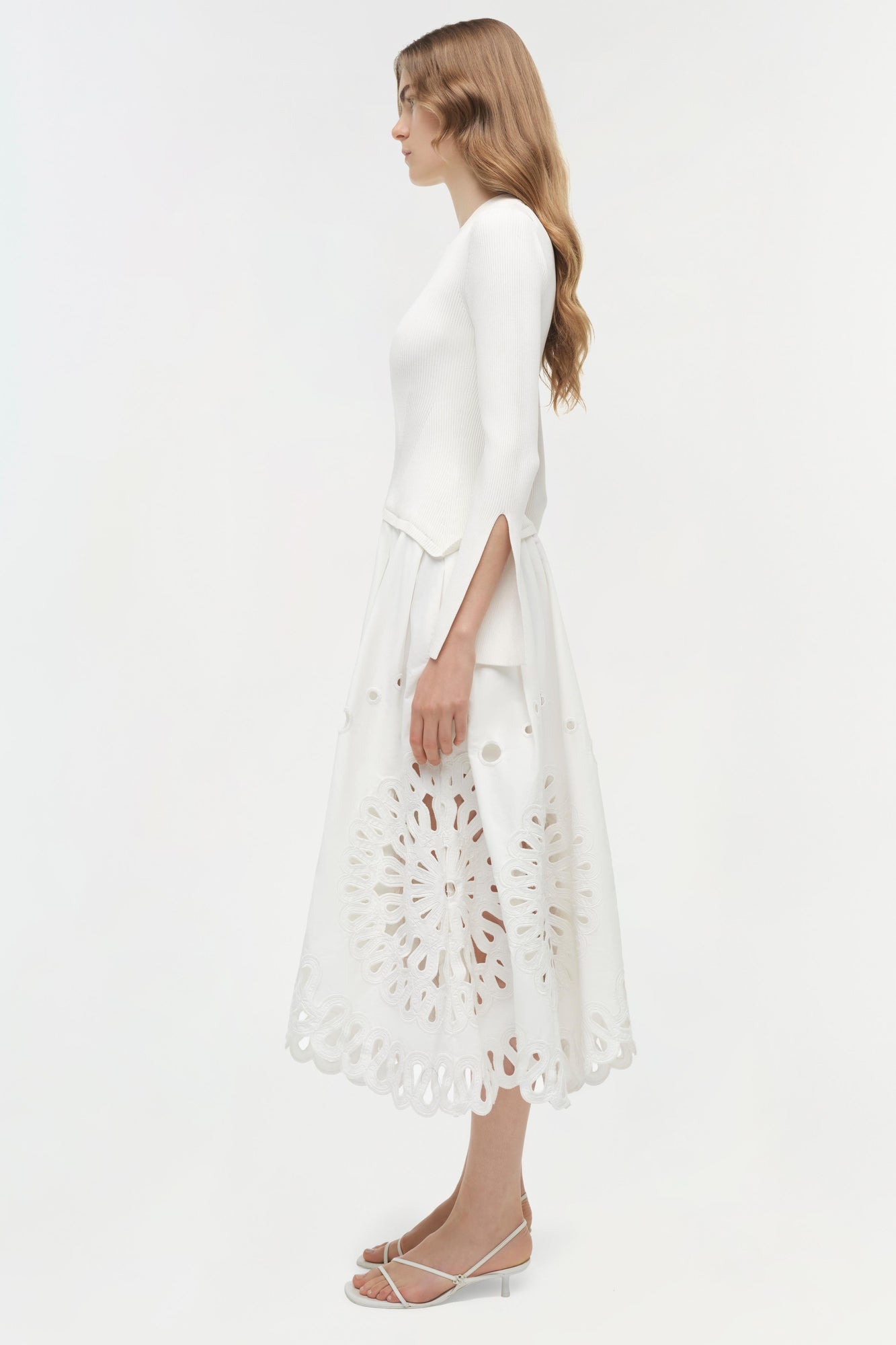 White knit midi dress with embroidered cutout circular pattern on skirt, modeled on woman in side profile view.