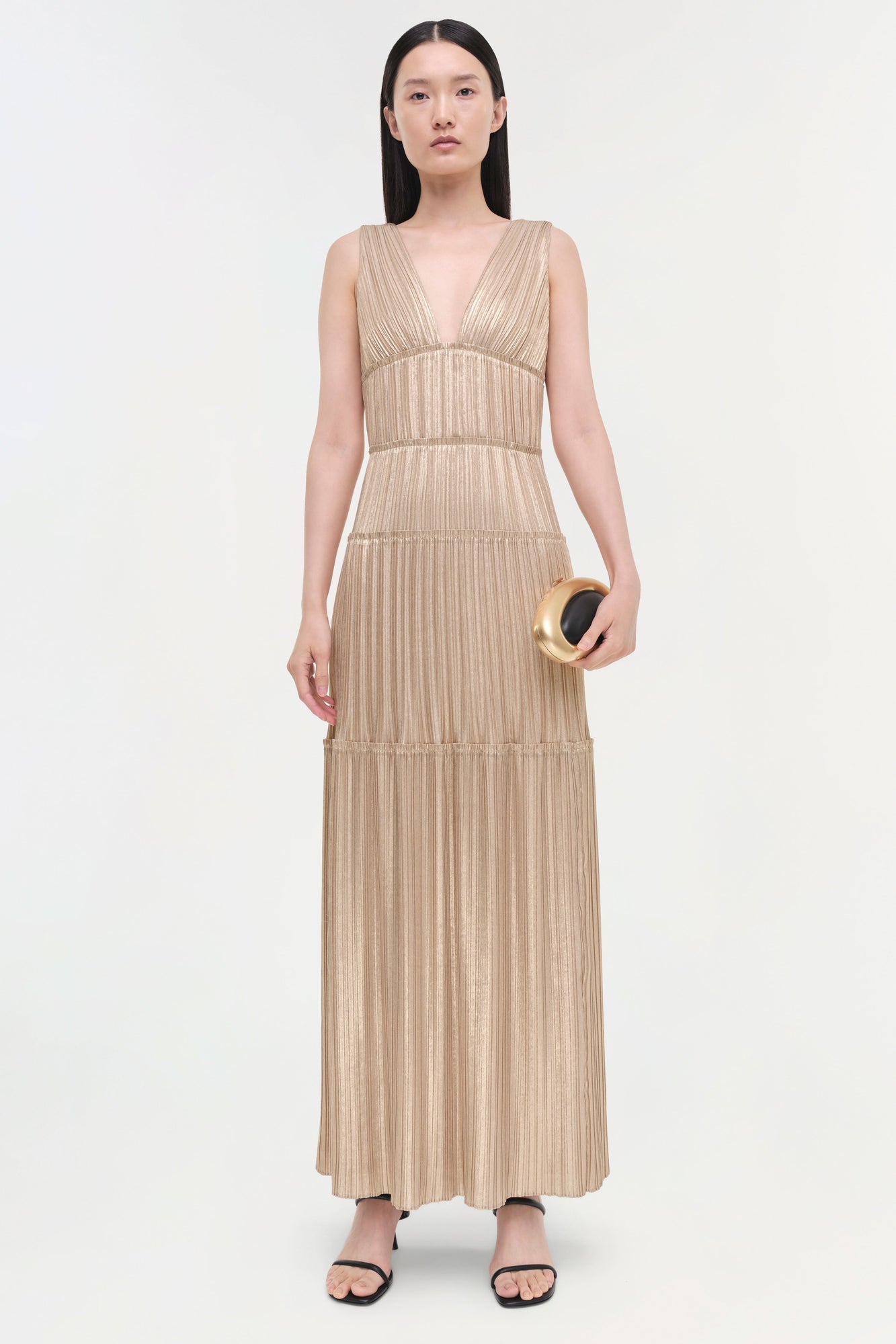 Beige pleated sleeveless gown with deep V-neckline, tiered waist bands, and full-length skirt.