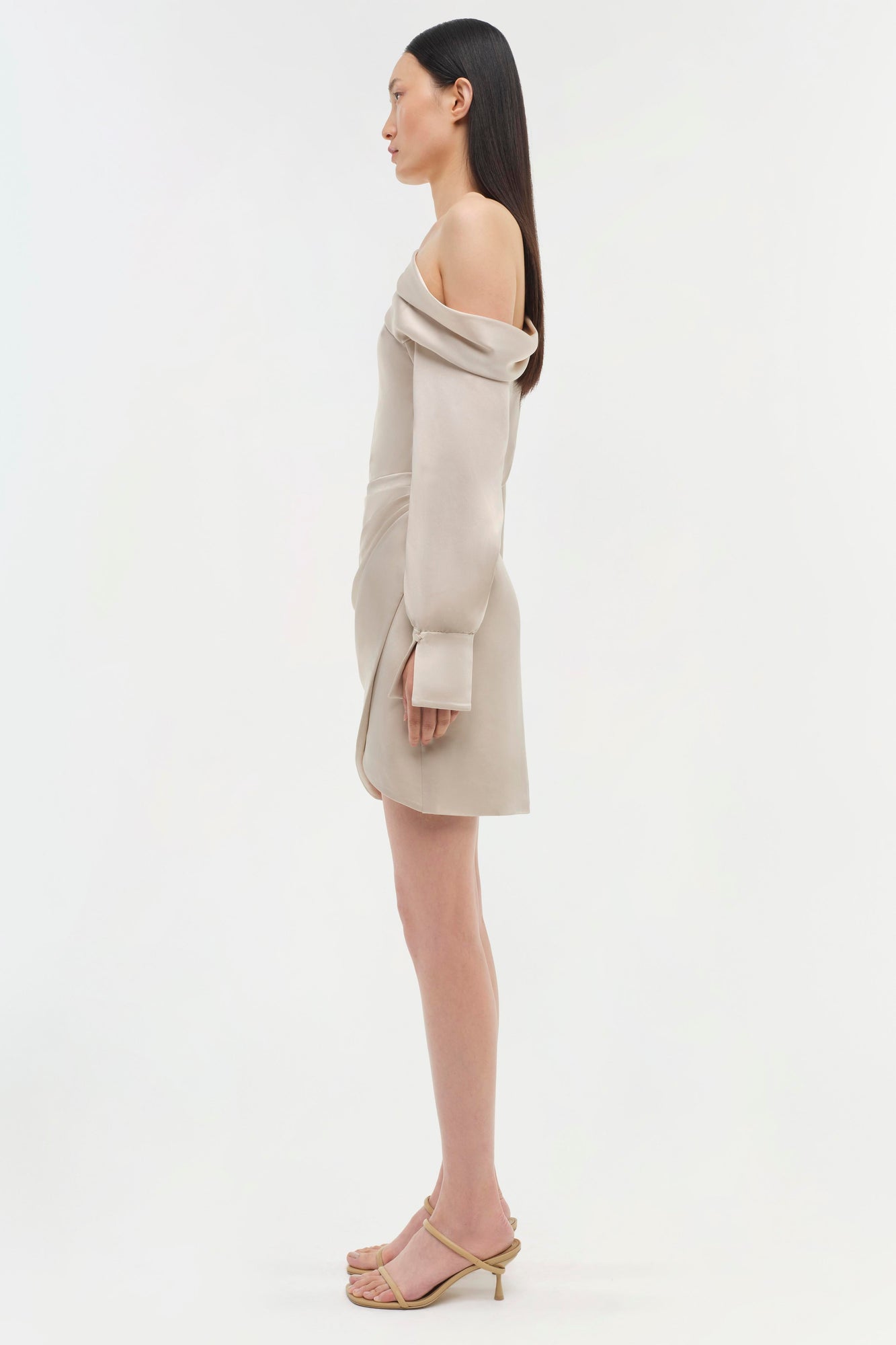 Cream off-shoulder dress with draped neckline and fitted sleeves, knee-length, shown on model from side profile.