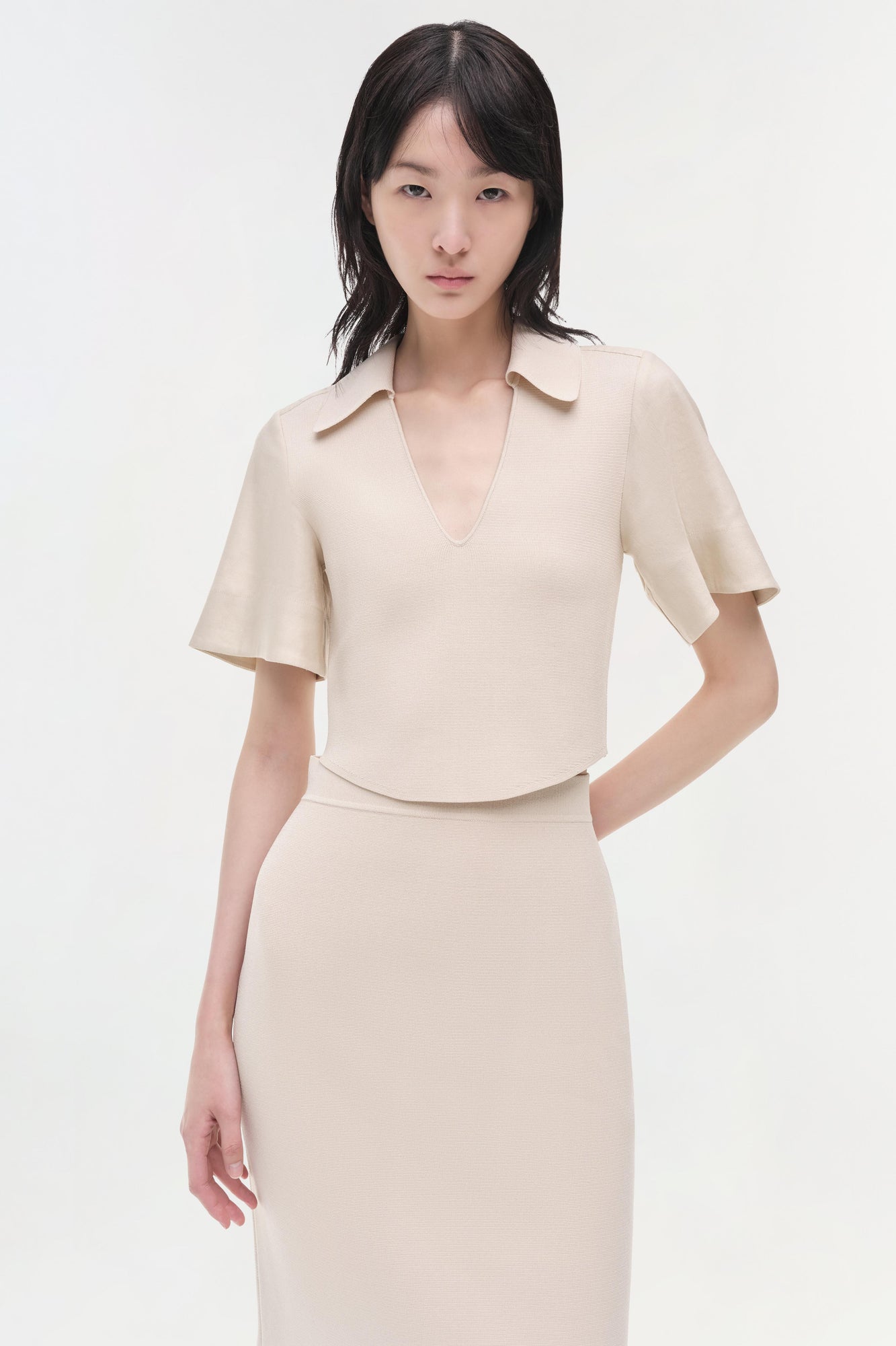 Beige linen knit midi skirt with high waist and side pockets, styled with matching short-sleeve collared top.