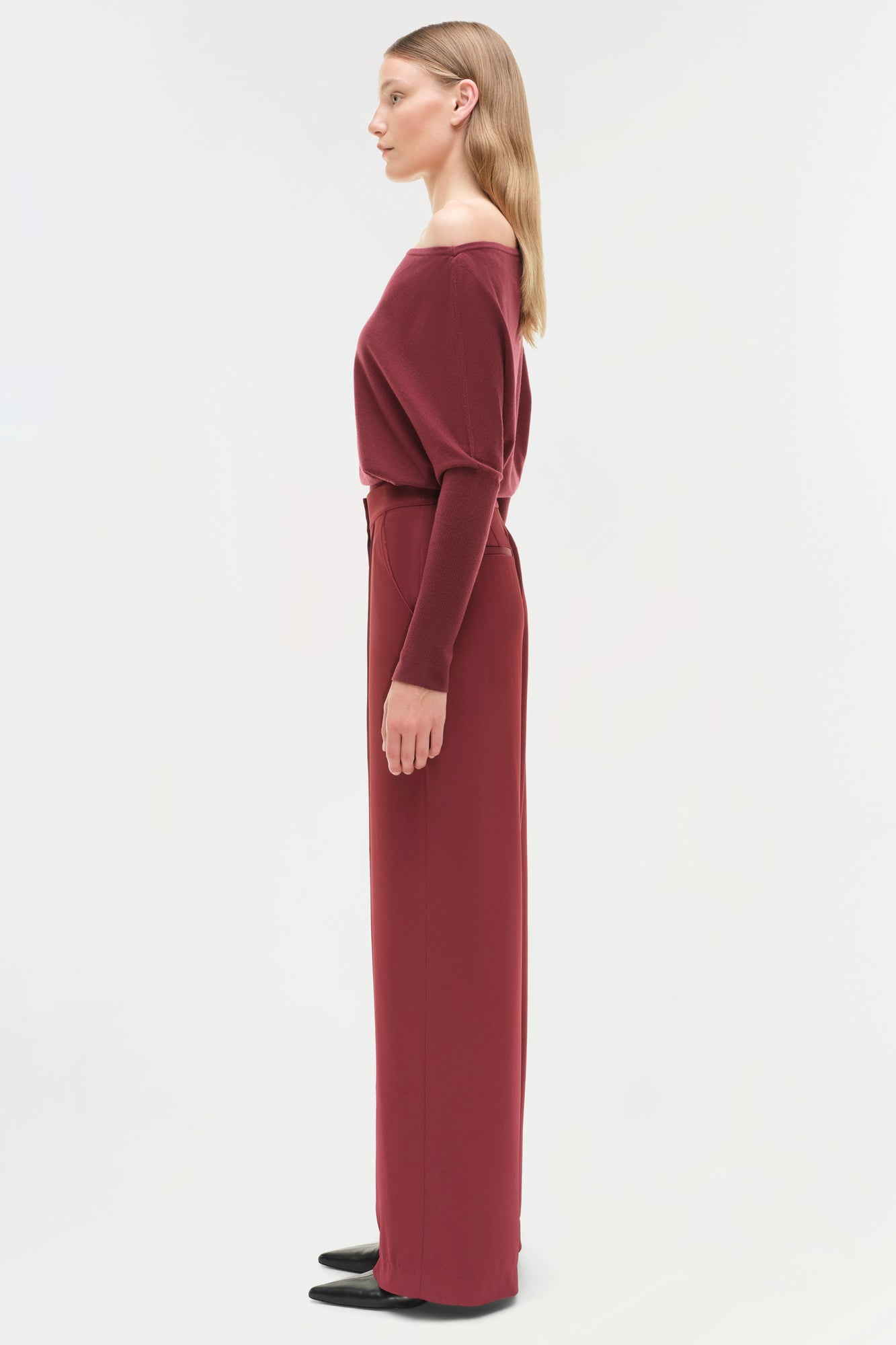 Burgundy off-shoulder sweater with long sleeves and wide-leg pants silhouette, shown from the side.