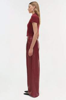 Woman wearing burgundy leather wide-leg pants with a matching short-sleeve top, shown in profile view.