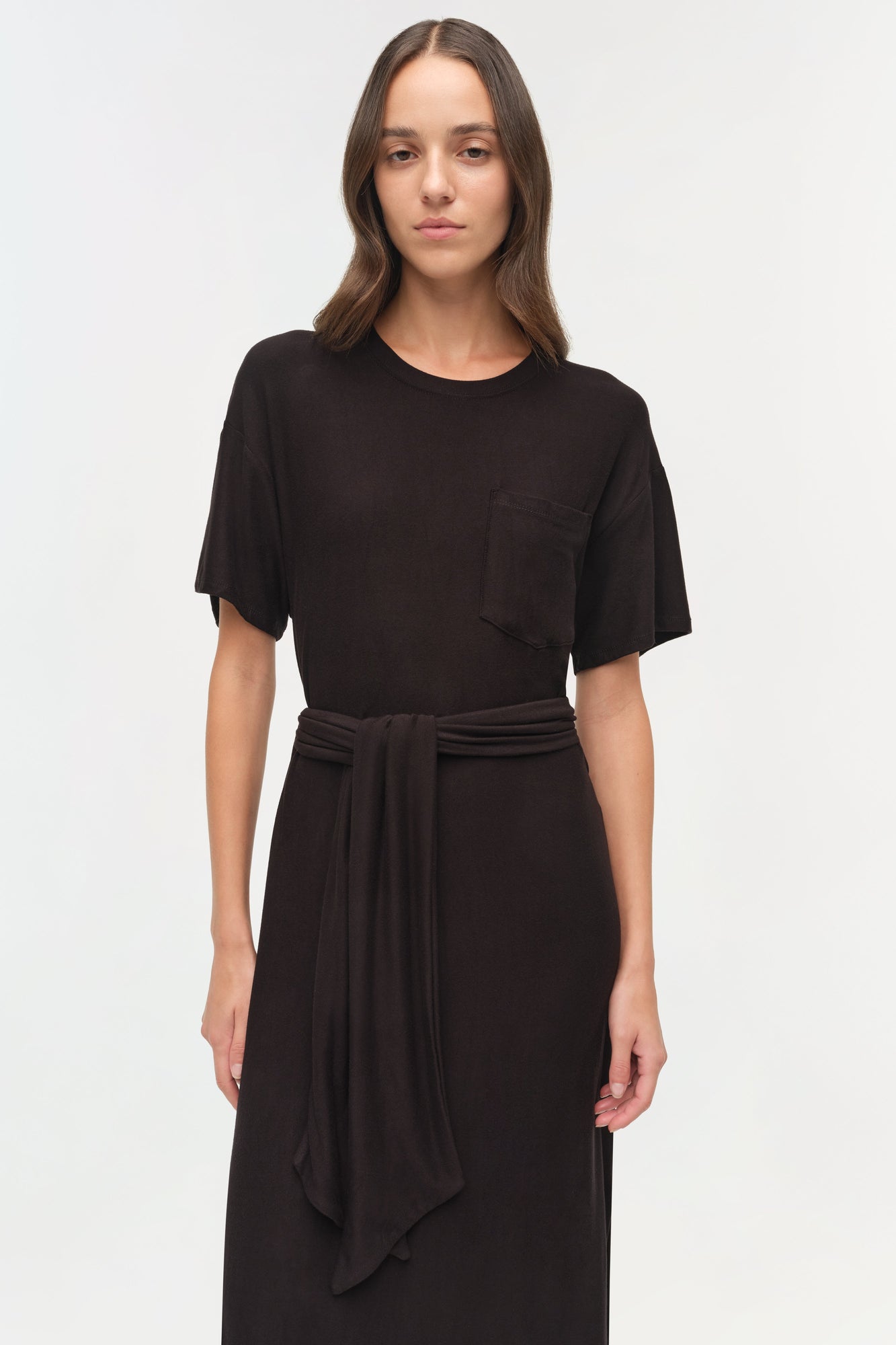 Black jersey t-shirt dress with short sleeves, chest pocket, and tie waist detail at center.