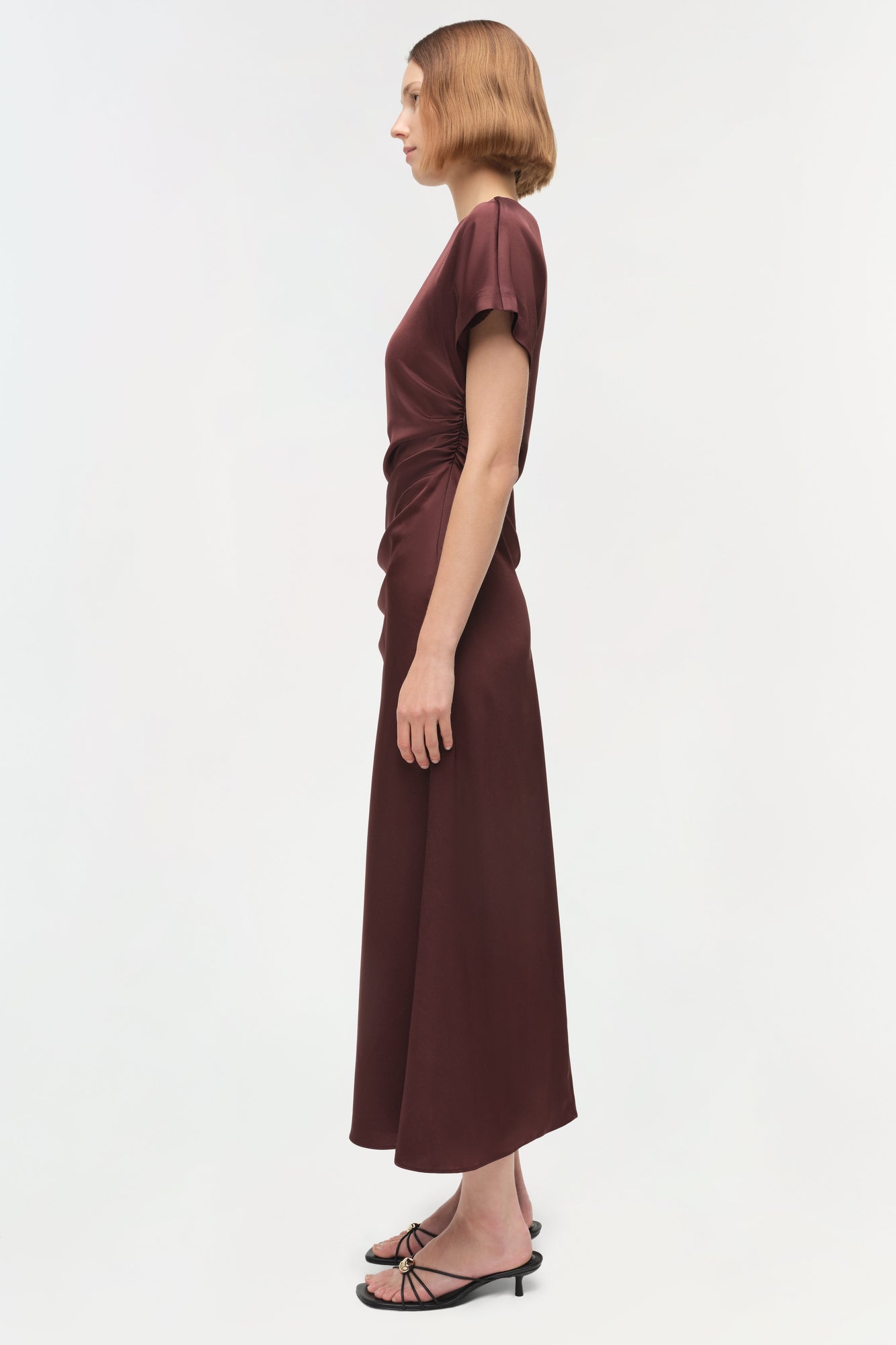 Burgundy satin midi dress with short sleeves and ruched side draping, shown on model in profile view.