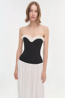 Woman wearing a strapless dress with a black corset bodice and white textured neckline trim, paired with a flowing cream skir