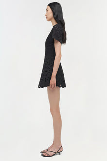 Black embroidered mini dress with short sleeves and scalloped hem, worn with black strappy heels.