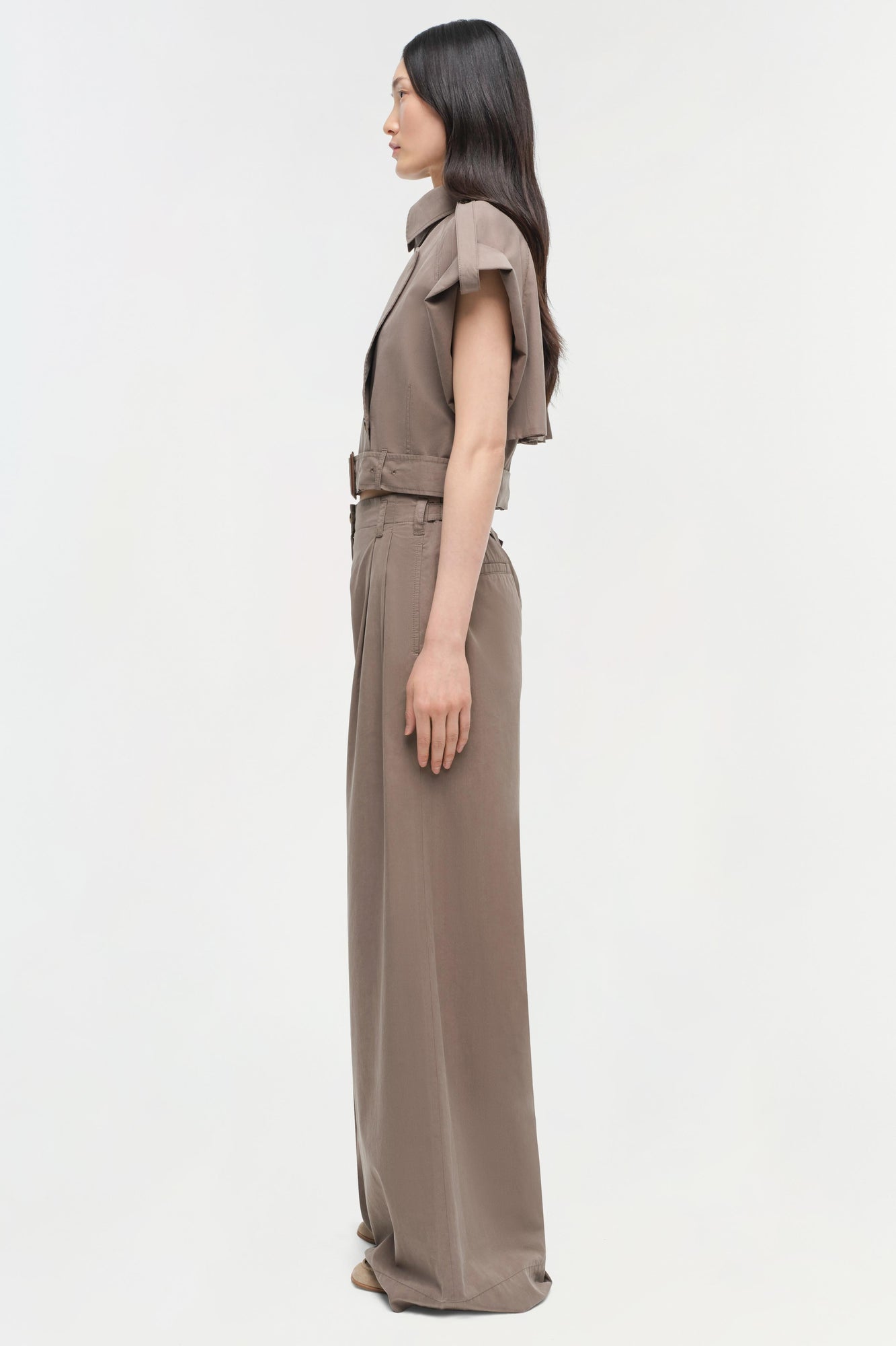 Woman wearing a taupe short-sleeved collared top with belt and matching wide-leg pants, shown in profile view.