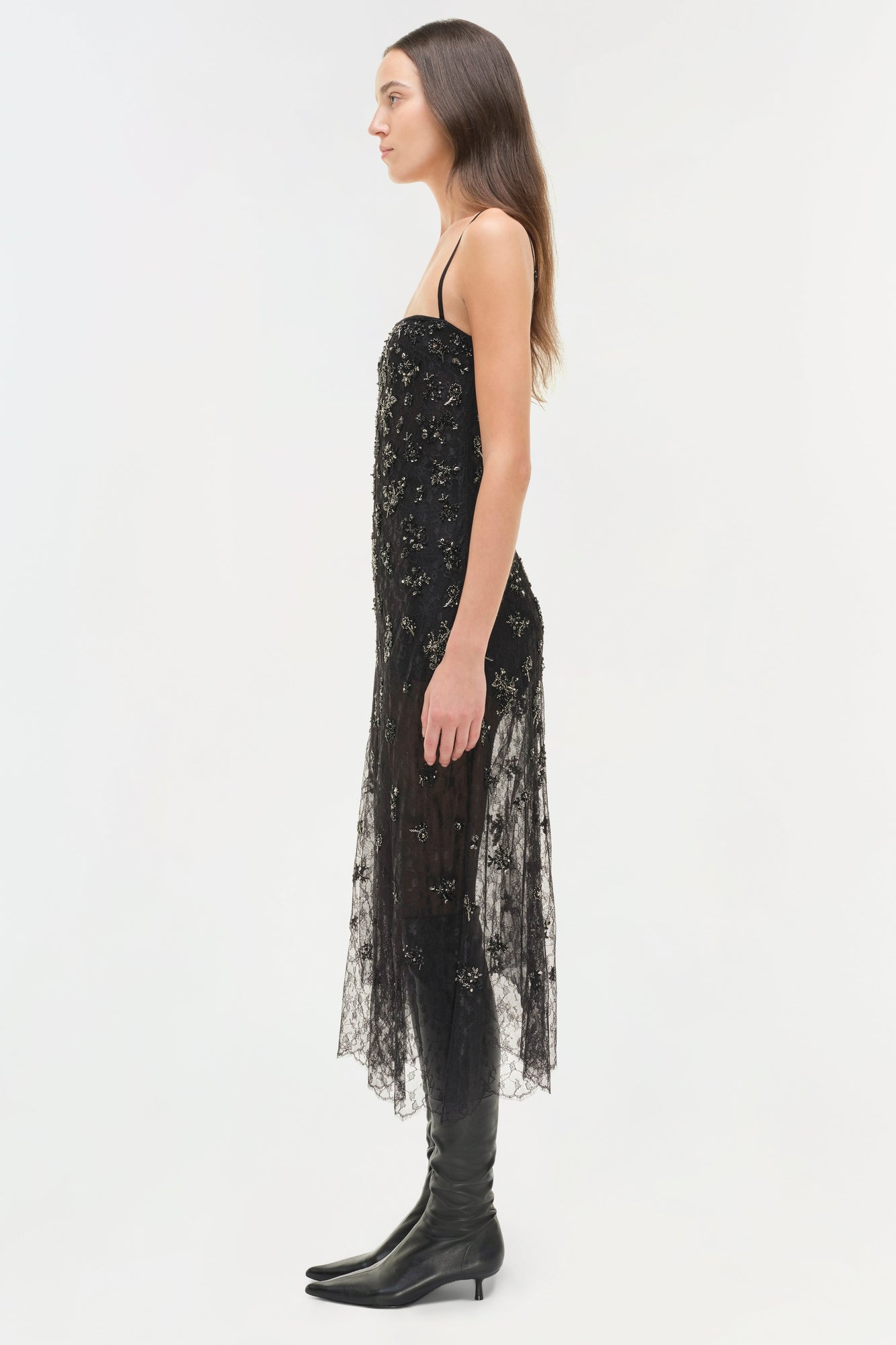 Black lace midi dress with beaded embellishments and asymmetrical hemline, worn with black knee-high boots.