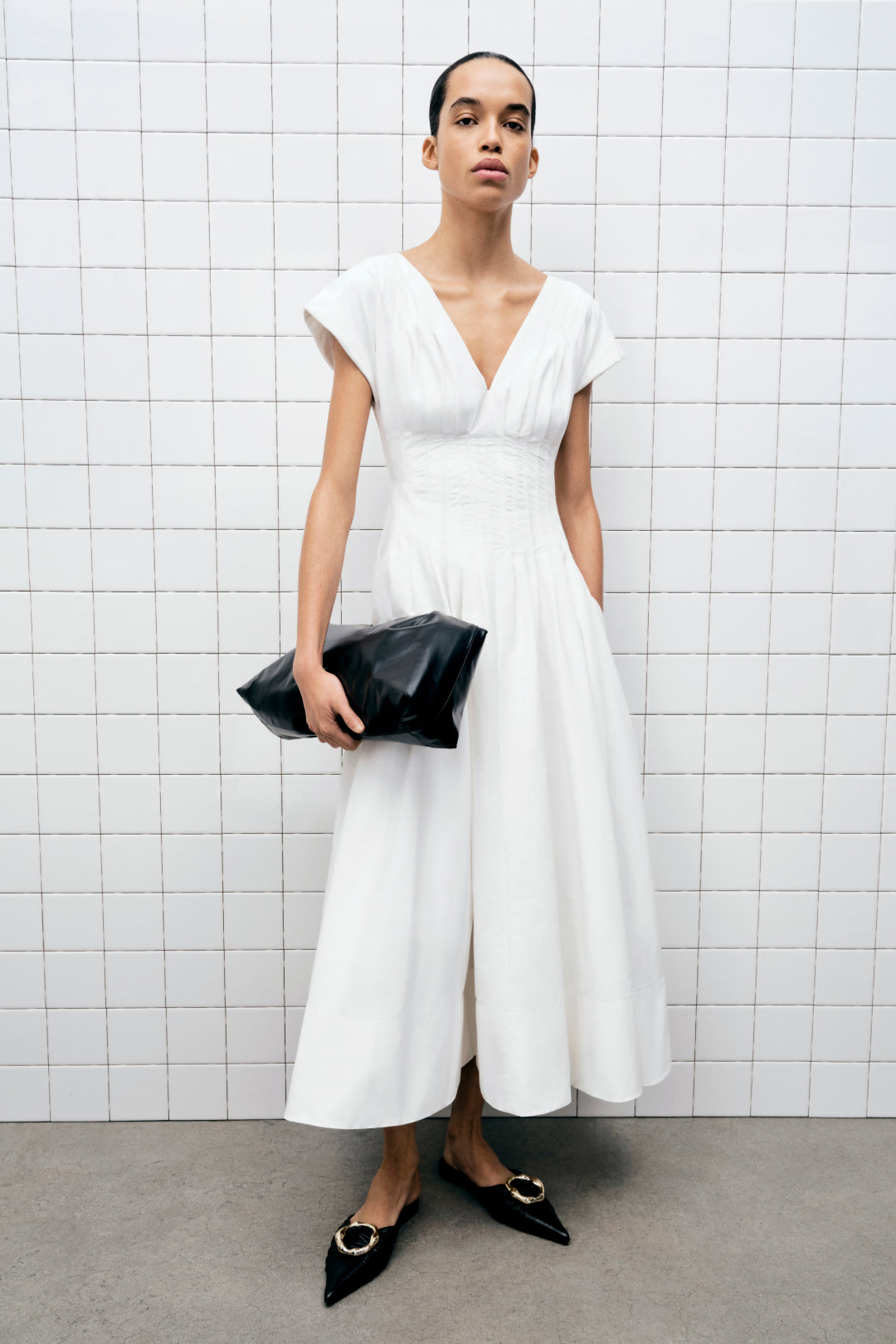 White cotton midi dress with V-neckline, short sleeves, and gathered waist on model wearing black pointed flats.