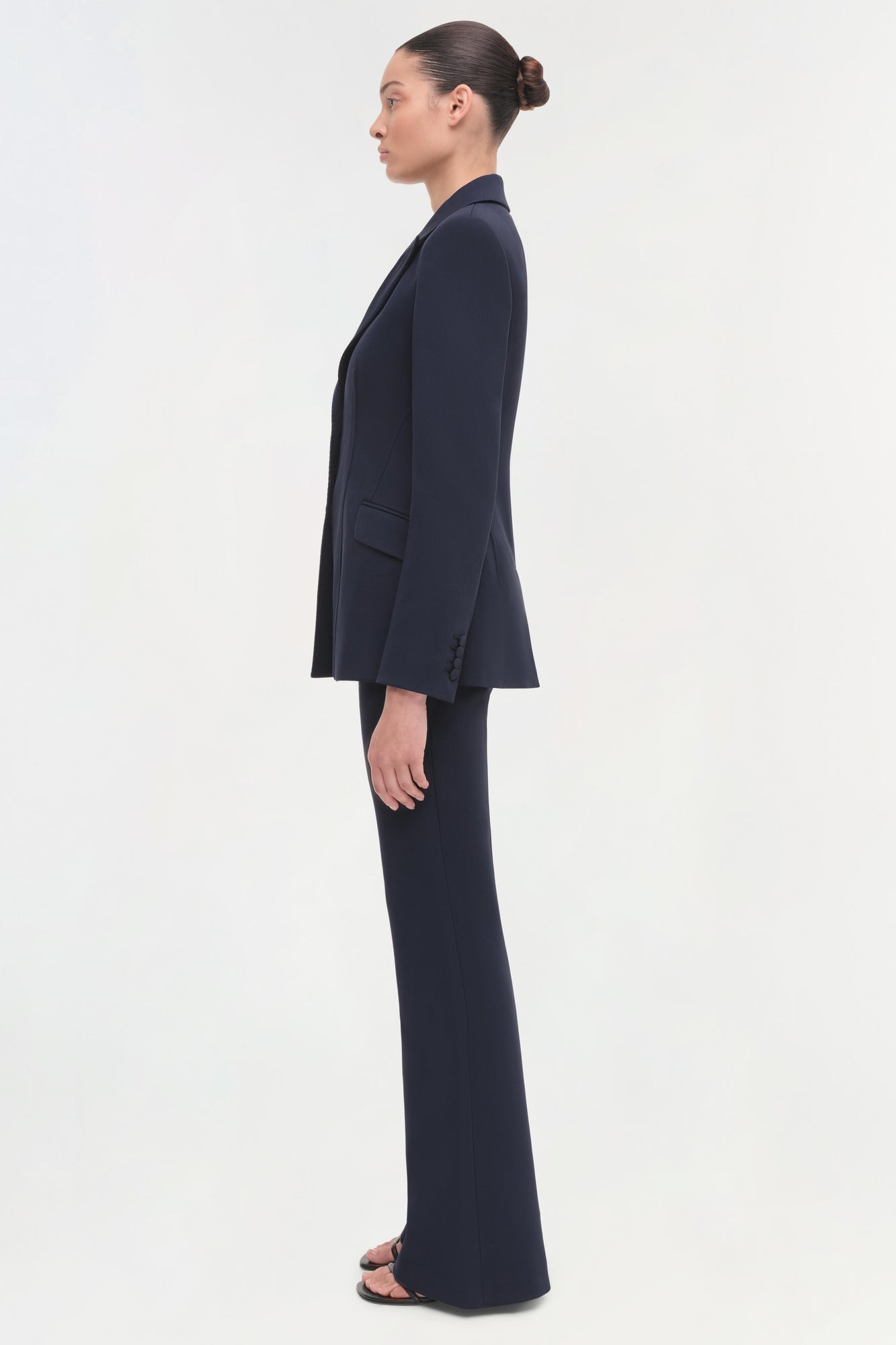 Woman wearing a navy single-breasted blazer with notch lapels and matching wide-leg trousers, shown in profile view.