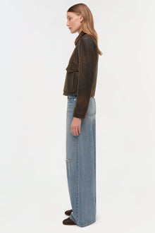 Woman wearing a sage-toned leather jacket with long sleeves and a collar, paired with light blue jeans.