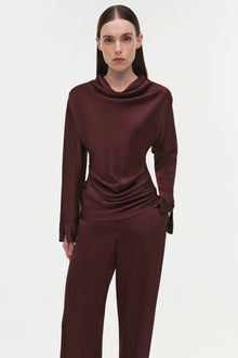 Burgundy draped satin top with cowl neckline and long sleeves on model wearing matching pants.