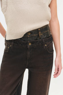 Black denim jeans with double waistband detail and brass hardware, worn with cream ribbed sweater.