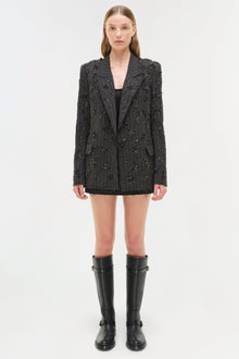 Black textured blazer with allover embellished beading and notch lapels worn with black knee-high boots.