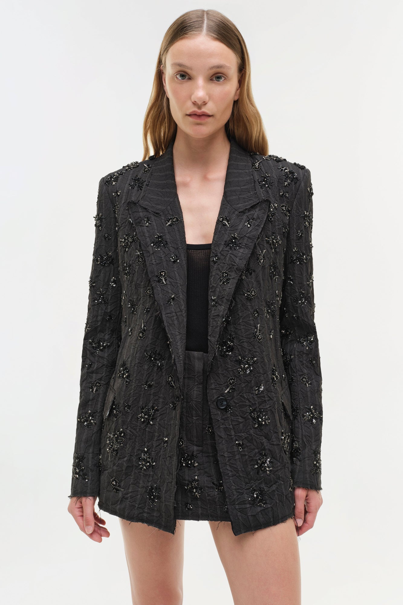 Black blazer with beaded embellishments and textured fabric throughout, worn open over a black top.