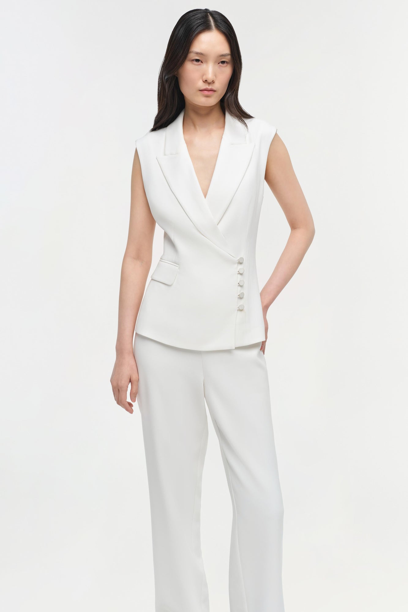 White straight leg trousers with high waist, worn with matching sleeveless blazer vest.