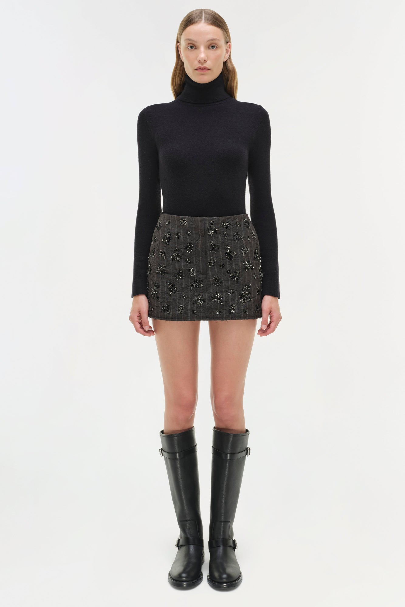 Black turtleneck sweater paired with gray embellished mini skirt and black knee-high boots.