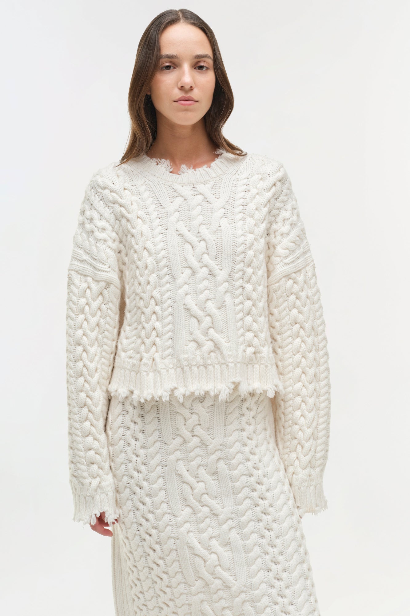 Cream cable-knit sweater with distressed edges and matching midi skirt with textured knit pattern.