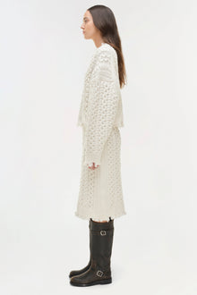 Cream cable-knit midi skirt with distressed details at thigh, worn with black buckled boots.