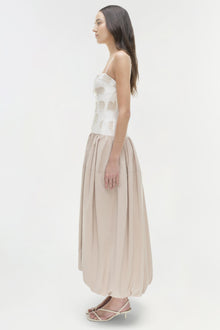 Woman wearing a sleeveless white cutout top with a beige gathered midi skirt, shown in side profile.