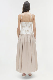 Woman wearing cream and beige midi dress with patterned bodice, thin straps, and pleated skirt, shown from back.