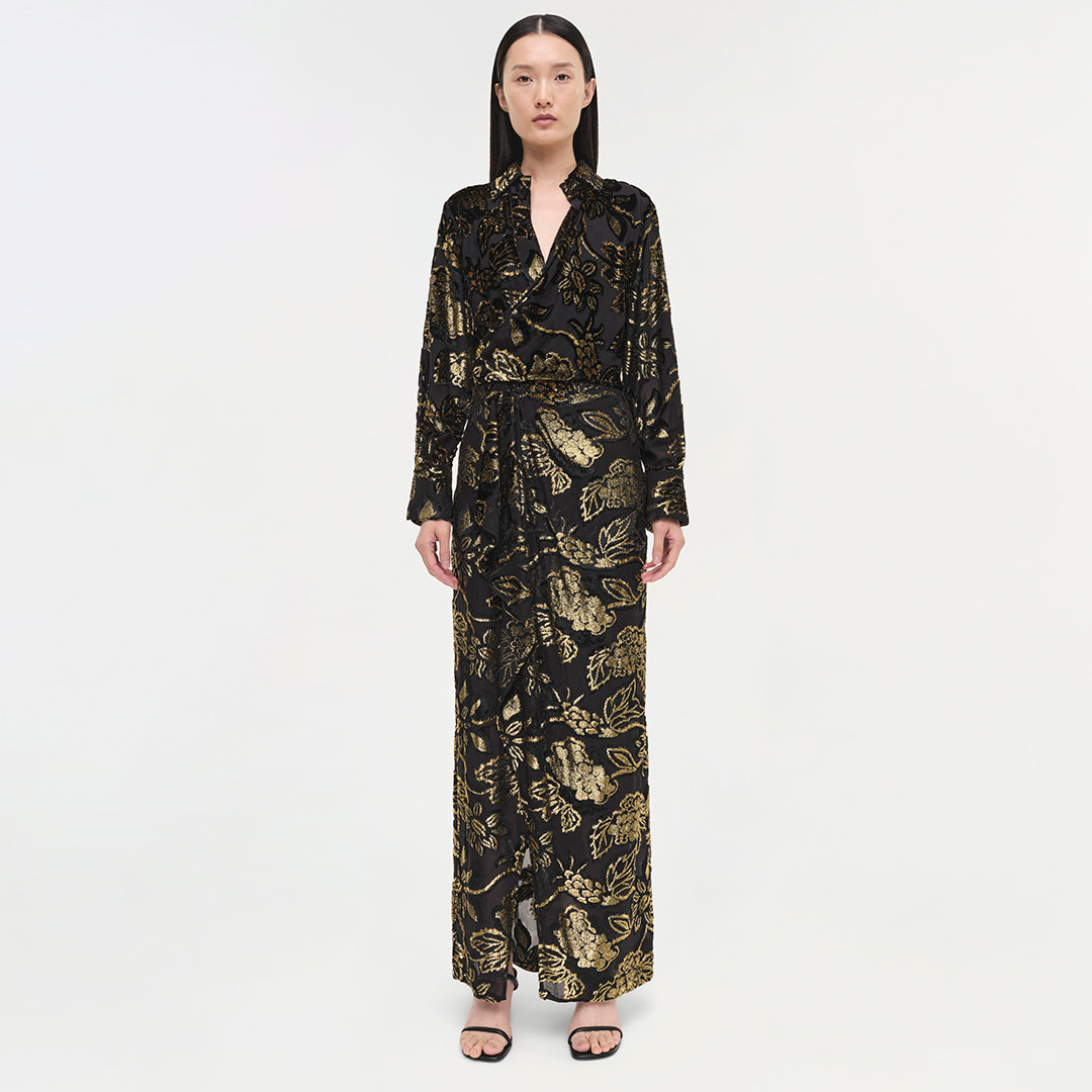 Black long-sleeve wrap gown with gold botanical print, full-length silhouette, worn with black slides.