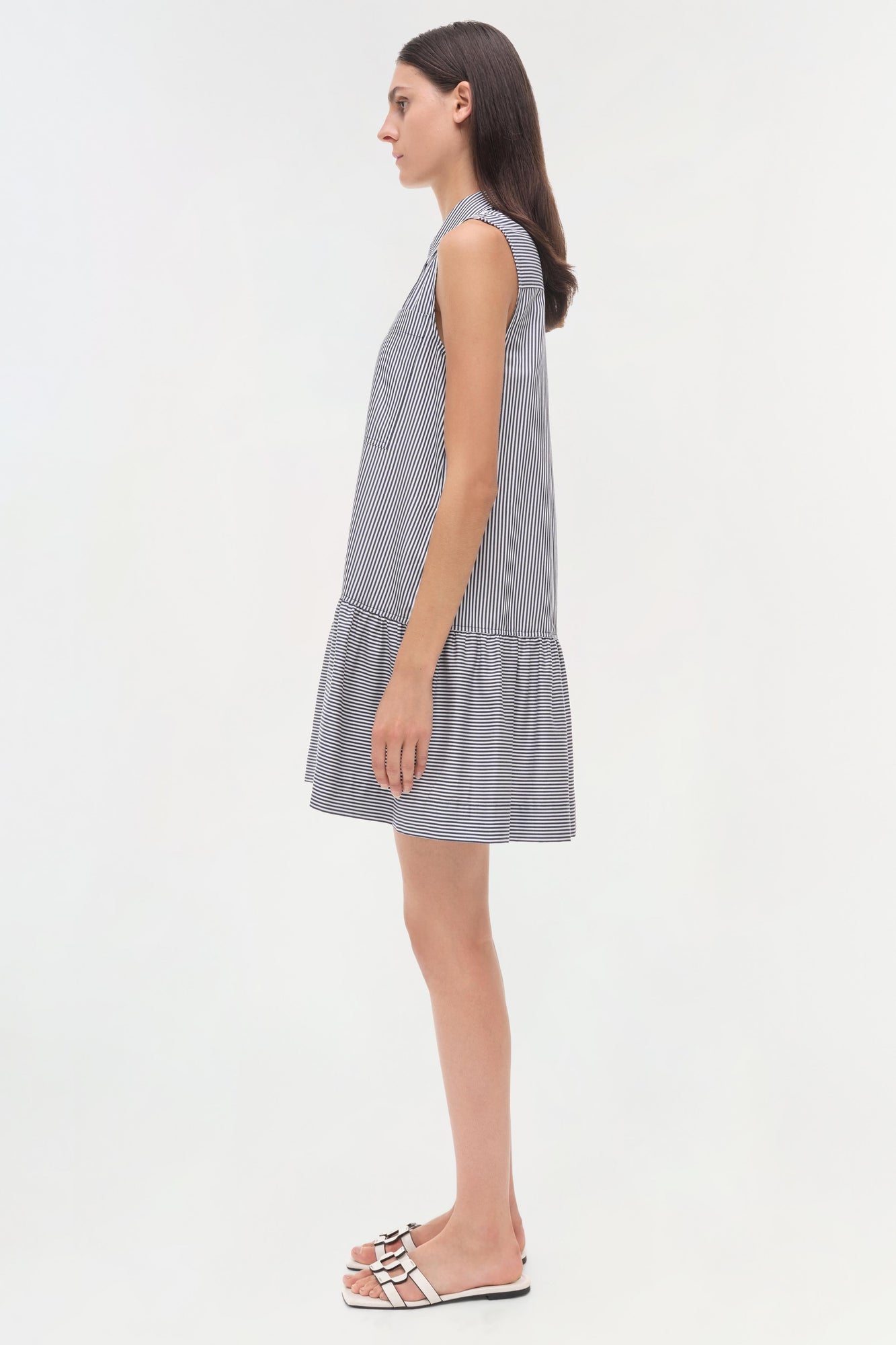 Woman wearing a sleeveless blue and white striped dress with a gathered hem, shown in side profile.