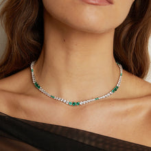 Close-up of a woman wearing a silver necklace with green gemstones.