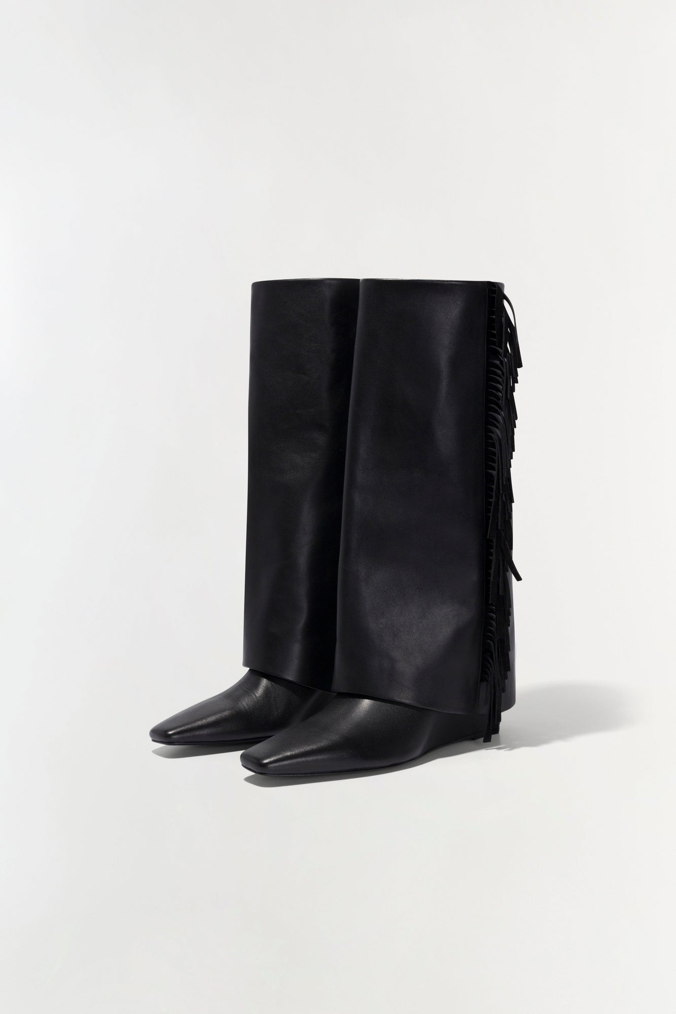 Black leather knee-high boot with fringe trim along the back shaft and pointed toe.