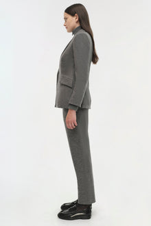 Woman wearing a gray wool blazer and matching trousers with black loafers, shown in profile view.