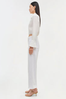 Woman wearing white cropped long-sleeve top with white wide-leg jeans and tan heeled sandals, shown in profile.