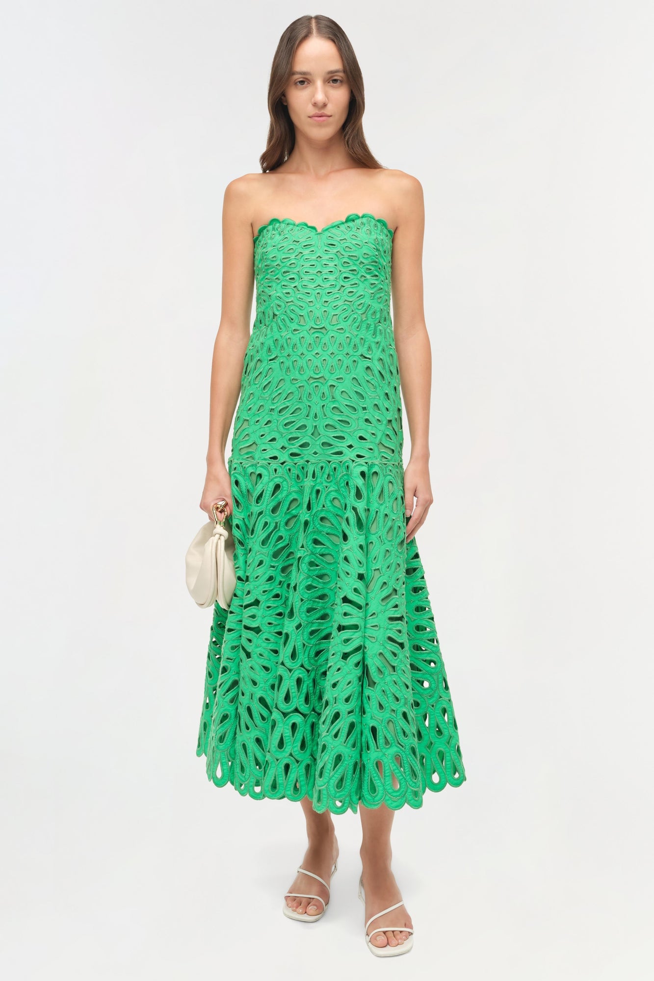 Woman wearing a green strapless midi dress with cutout embroidered pattern and tiered skirt.