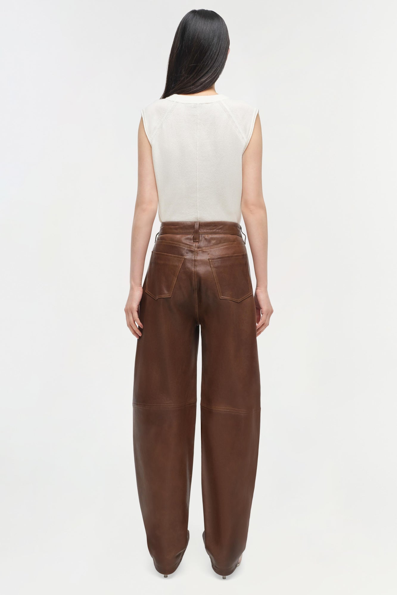 Cream sleeveless cashmere vest with crew neckline, shown from back on model wearing brown leather pants.
