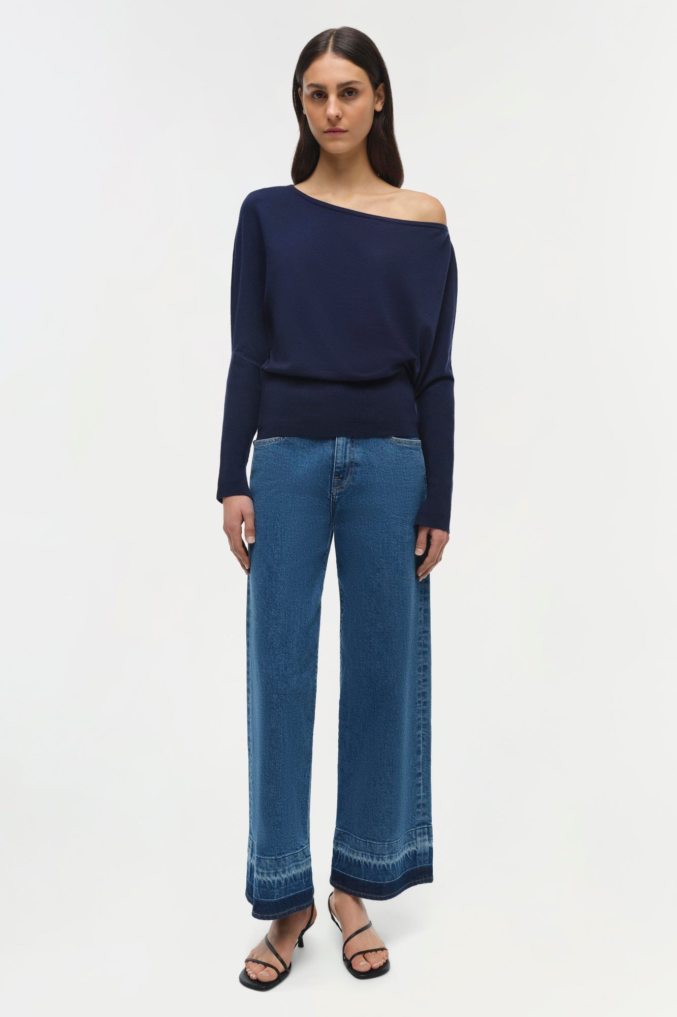 Navy off-shoulder sweater with long sleeves and cropped length worn with blue jeans.