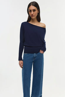 Navy off-shoulder sweater with long sleeves and ribbed waistband worn with blue jeans.