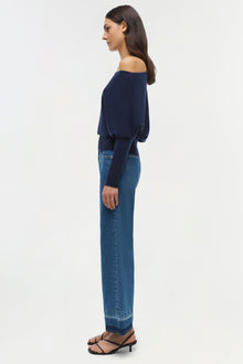 Woman wearing off-shoulder navy sweater with long sleeves and blue jeans, shown from side profile.