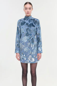 Blue dress with silver floral print, mock neckline, long sleeves, and wrap-style waist detail.