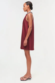 Burgundy satin sleeveless shift dress with embellished neckline, shown on model in profile view.