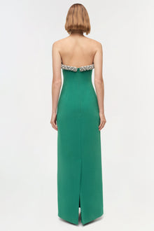Woman wearing a green strapless gown with crystal embellishments at the neckline and a center back slit, shown from behind.