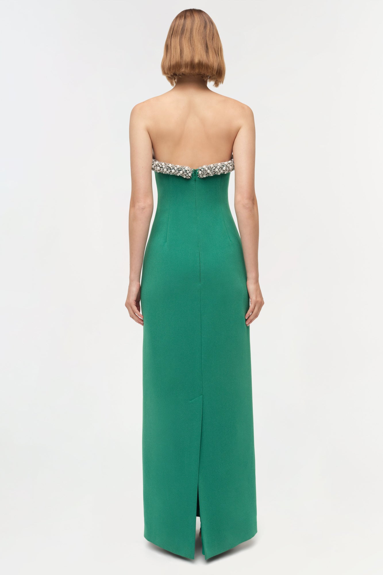 Woman wearing a green strapless gown with crystal embellishments at the neckline and a center back slit, shown from behind.
