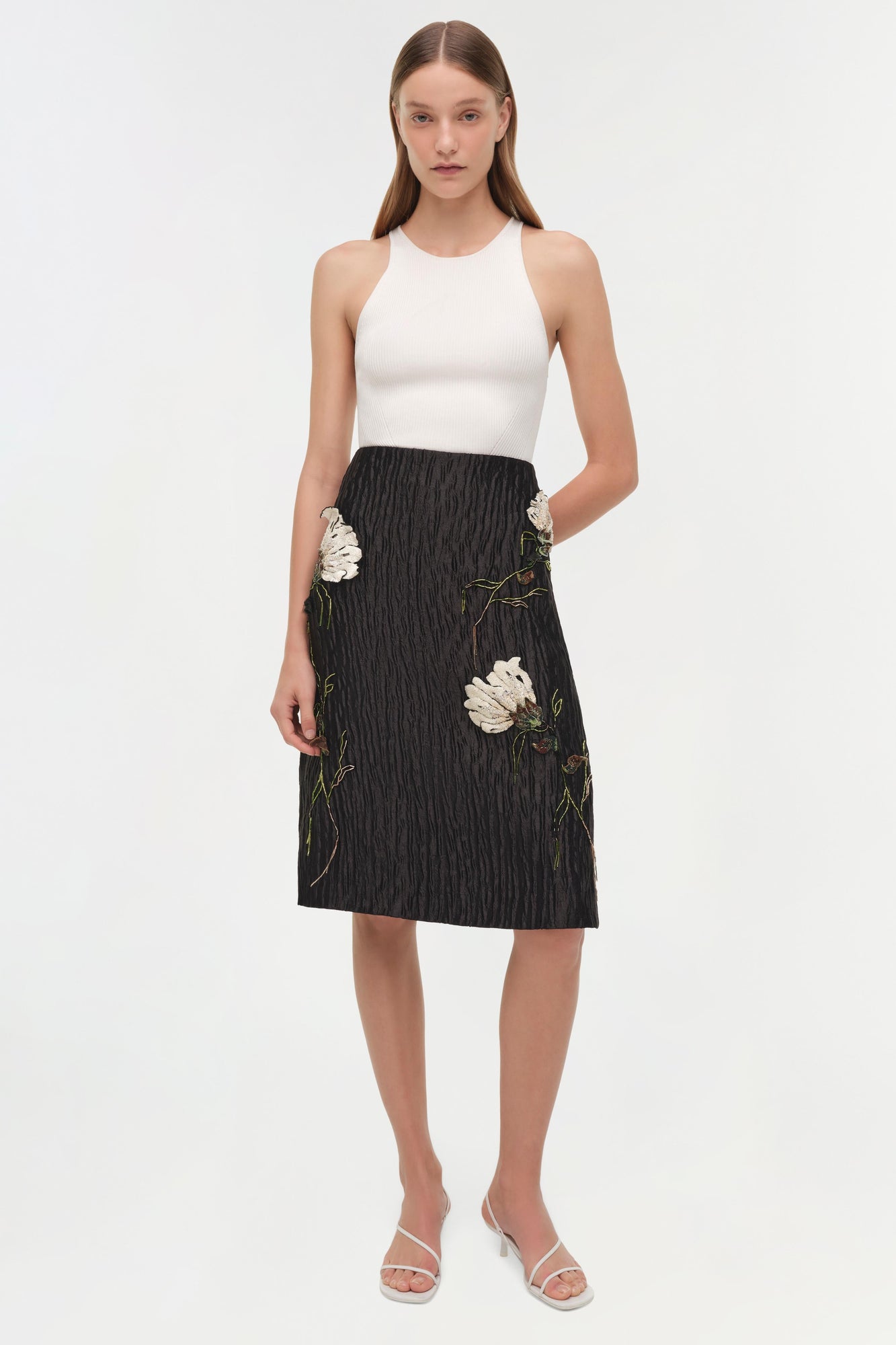 Black midi skirt with white floral jacquard pattern and side pockets, paired with white sleeveless top.