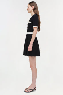 Black ribbed knit mini dress with white trim at neckline and waist, short sleeves, and pleated skirt.