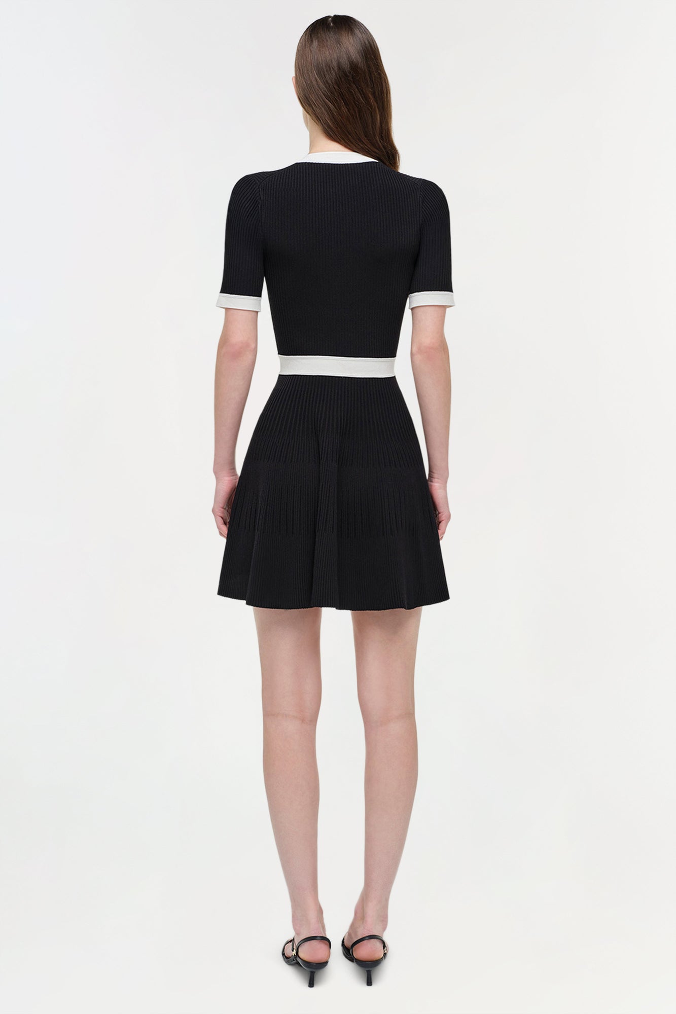 Black ribbed knit mini dress with white trim at neckline, cuffs, and waistband, shown on model from back.