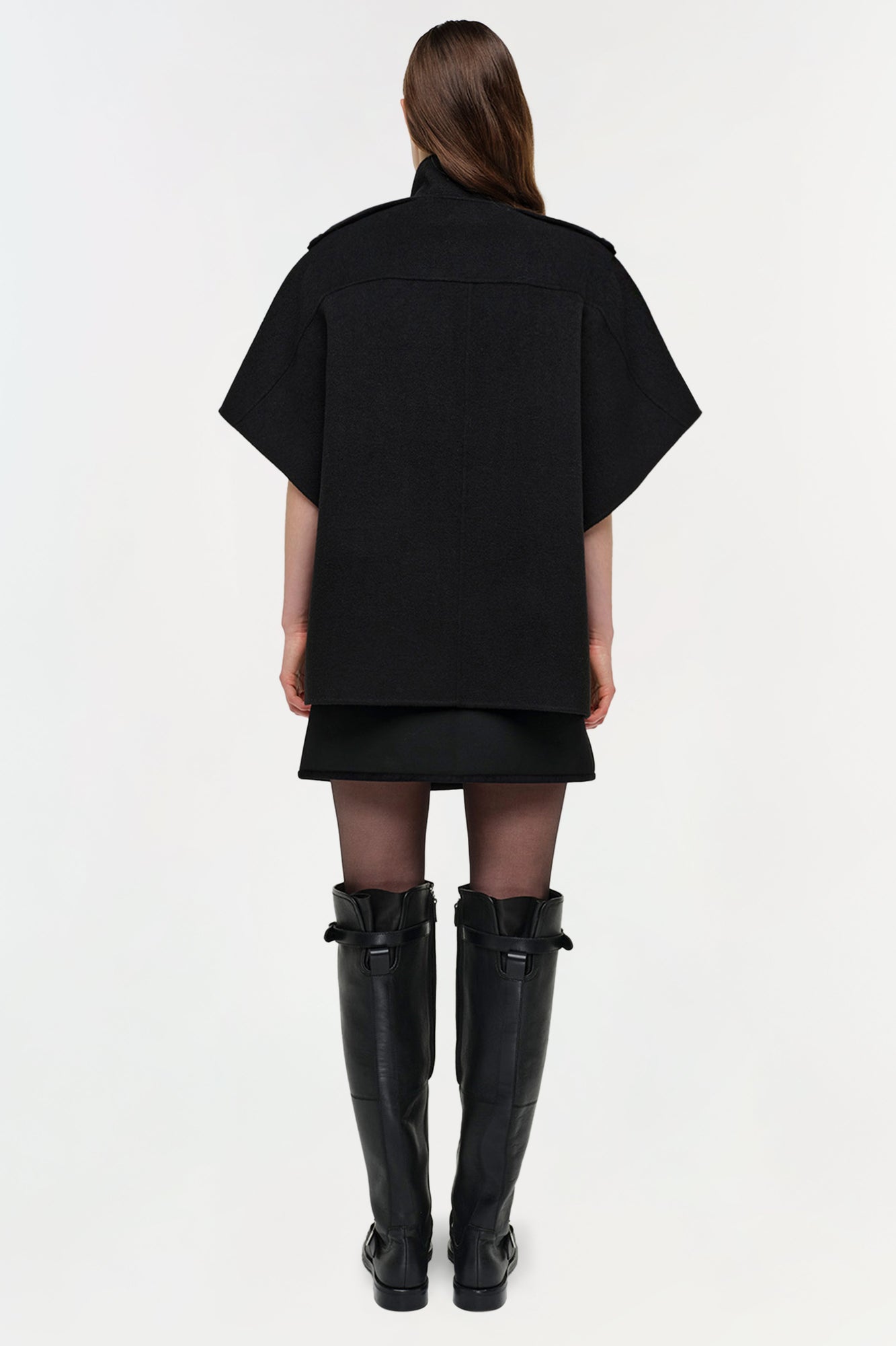 Black wool cape jacket worn over a black dress with knee-high black boots, shown from back view.