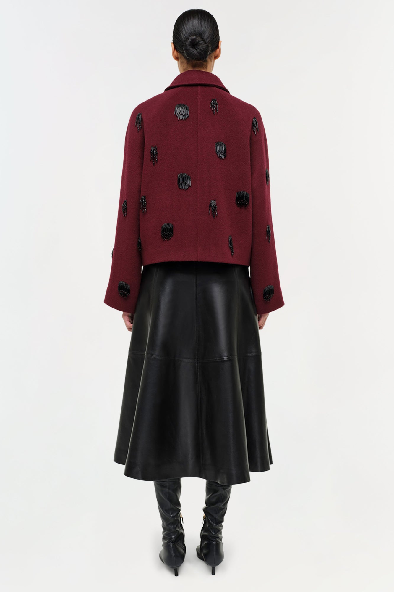 Black leather midi skirt with A-line silhouette worn with burgundy patterned jacket and black boots.