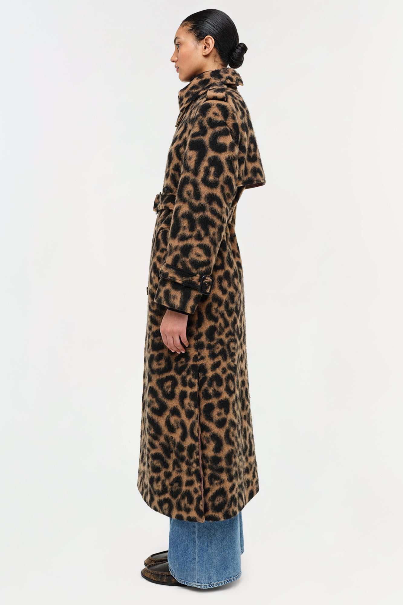 Woman wearing a long leopard print wool overcoat with a collar, button front, and cuffed sleeves over blue jeans.