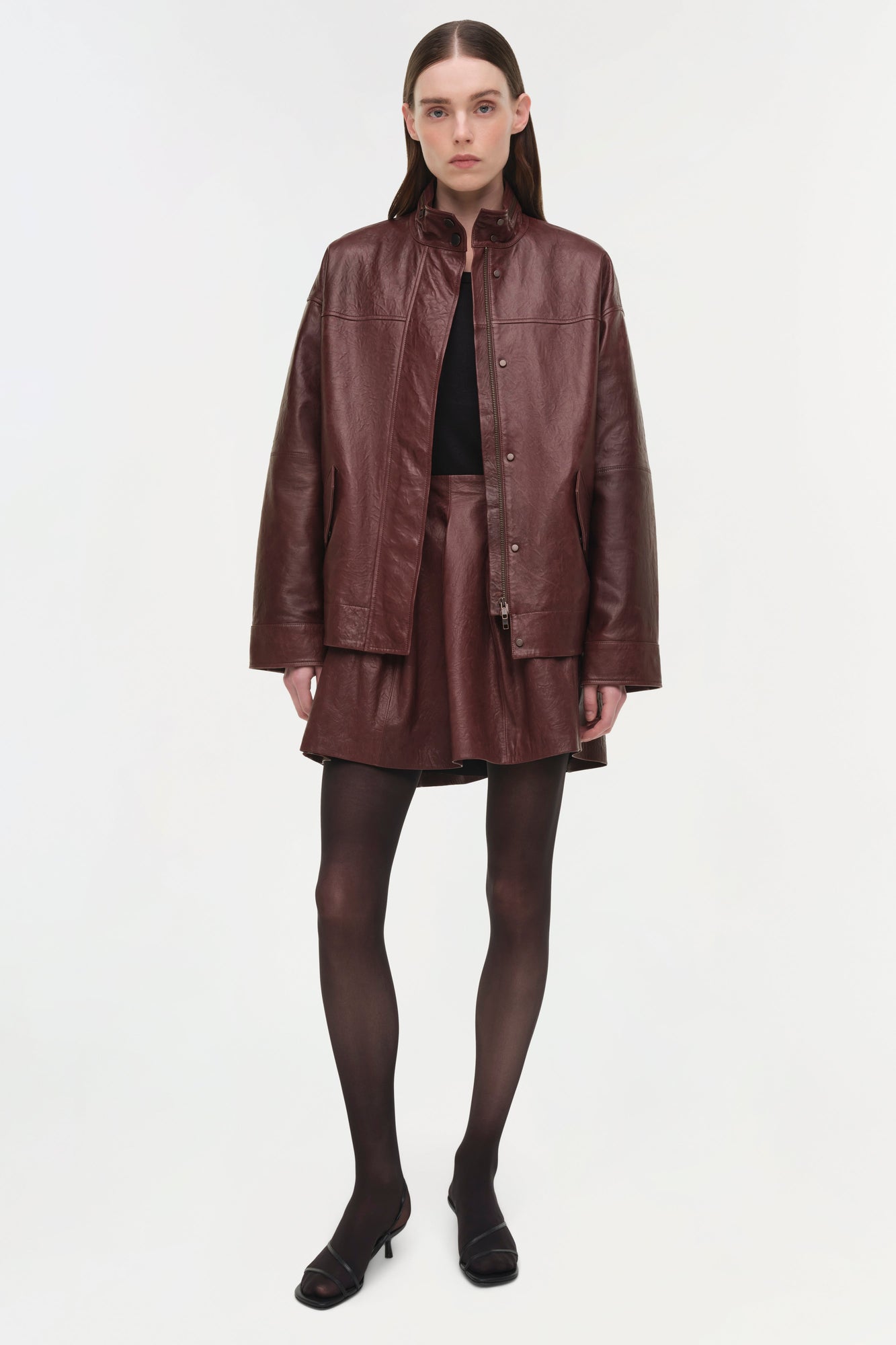 Burgundy leather jacket with button front and collar, worn open over a black top and matching skirt.