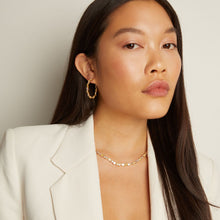 Model. Woman wearing gold earrings and necklace against a neutral background