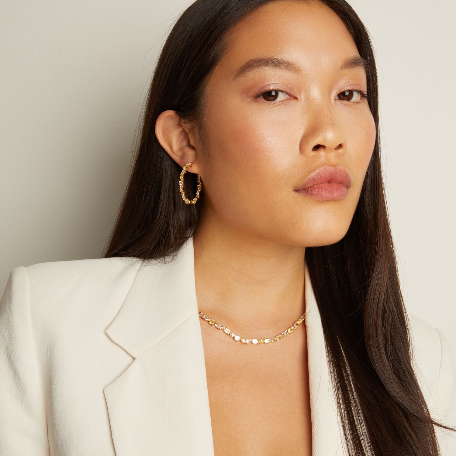 Model. Woman wearing gold earrings and necklace against a neutral background